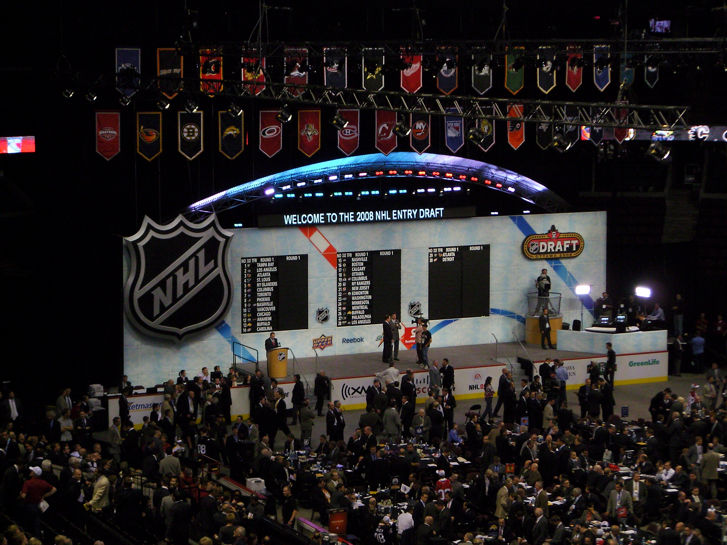 The draft floor — the pick board lit up on stage before rows of GM tables.
